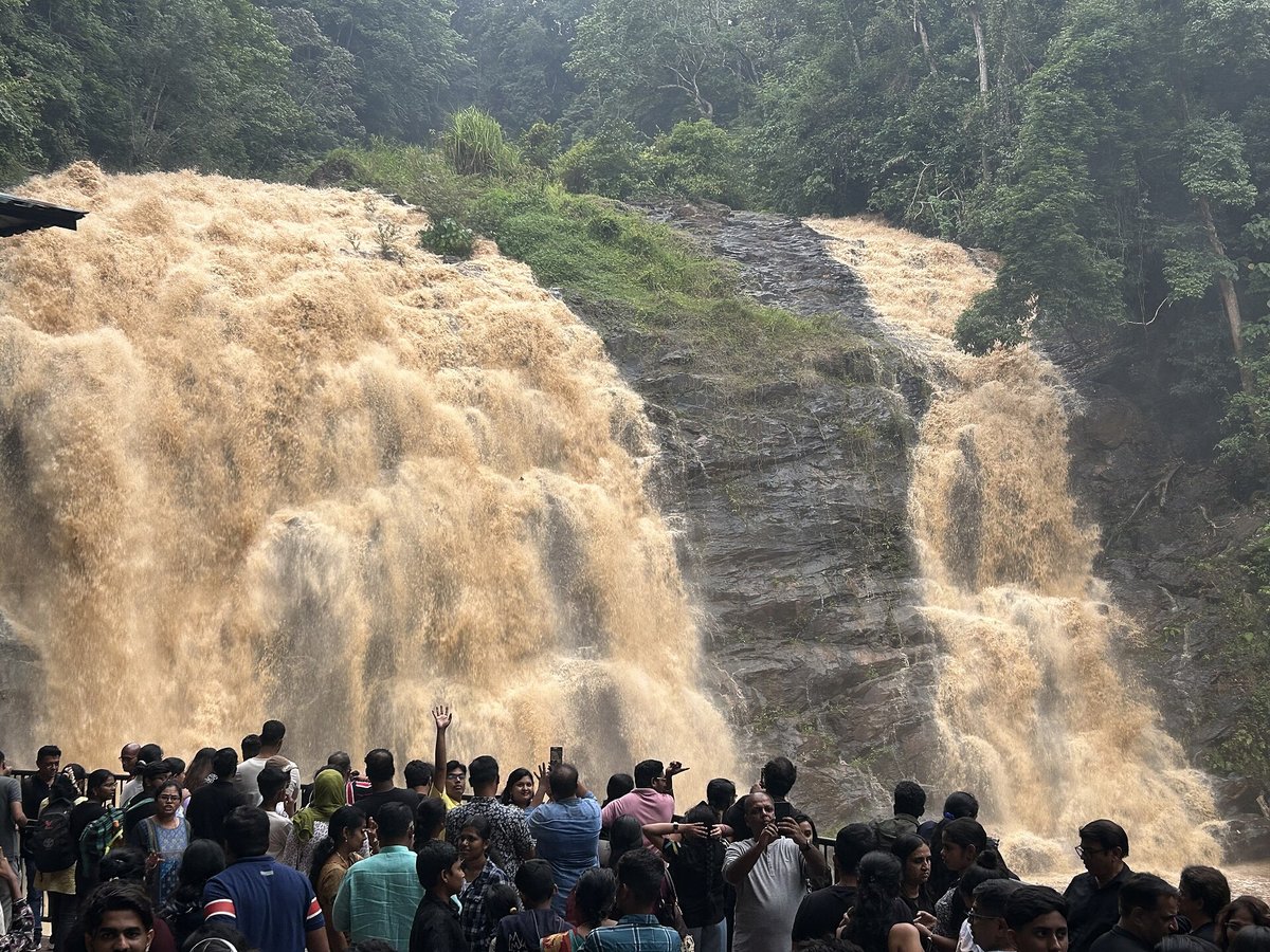 Abbey Falls Coorg Entry Fee 2026: Timings, Hanging Bridge, Rules and How to Reach Crowd of visitors at the railing of the Abbey Falls viewing area as the falls run high and muddy brown over a dark rock face