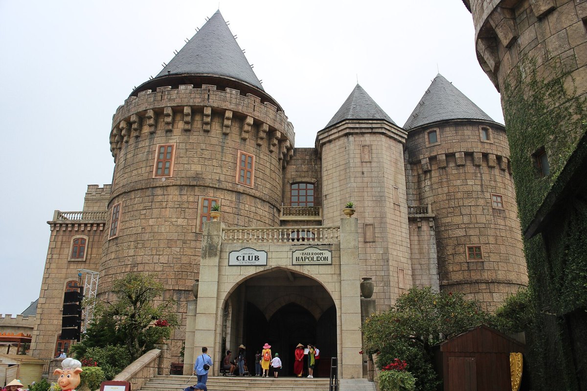 Ba Na Hills Ticket Price: Cable Car, Golden Bridge Access and Buffet Combos Explained Stone castle with grey turrets and an arched entrance in the French Village at Ba Na Hills, Da Nang