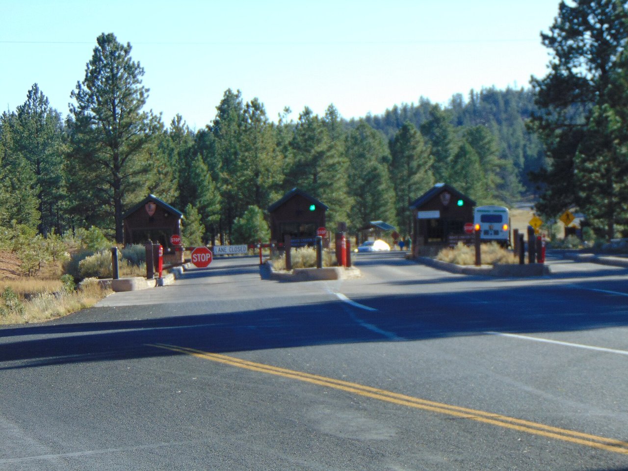 Three wooden entrance booths with stop signs across the park road at the Bryce Canyon National Park entrance station, among tall pine trees