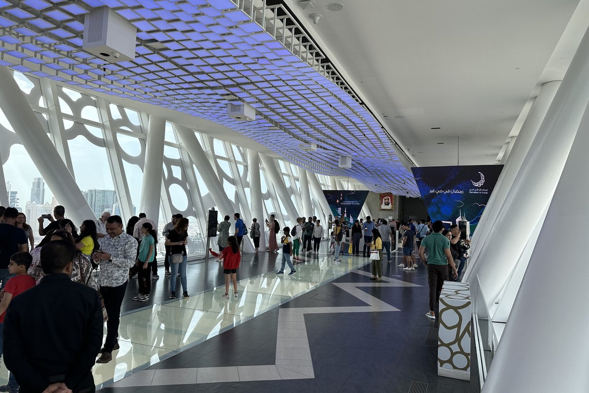 Visitors walking along the Sky Deck bridge of the Dubai Frame with white lattice windows and a blue-lit ceiling