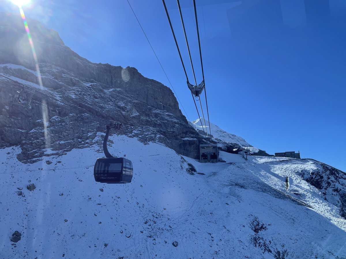 A cabin of the Eiger Express tricable gondola travelling up a snowy slope below the rock face of the Eiger, with the Eigergletscher station ahead