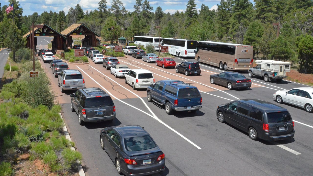 Lines of cars and tour buses waiting at the wooden entrance booths of the Grand Canyon South Entrance Station among pine trees
