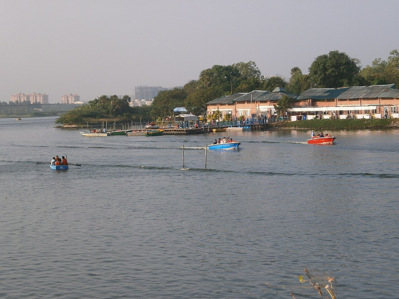 Muttukadu boat house buildings among trees on the backwater, with small boats on the water in front