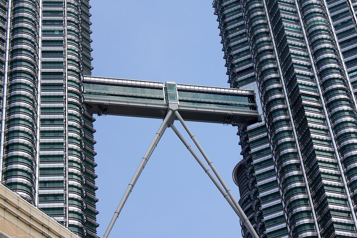 The double-decker Skybridge between the two Petronas Twin Towers, with its angled support legs, seen from below against a blue sky